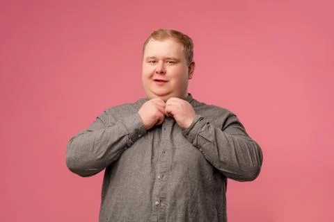 Glad cheerful man looking at camera while buttoning hig grey shirt on pink Foto stock