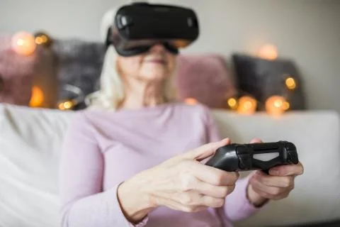 Glad senior lady using vr headset holding controller Stock Photos