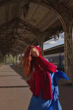 Glad young smiling red-haired European woman in red coat and blue dress dancing Stock Photos