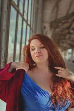 Glad young smiling red-haired European woman in red coat and blue dress at train Stock Photos