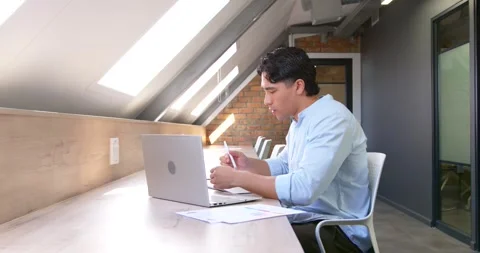 Glancing at papers for review, man typing on laptop, using pen, noting at Stock Footage 342030927