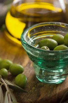Glas cup of olives with extra virgin olive oil in glass bottle on rustic back Stock Photos