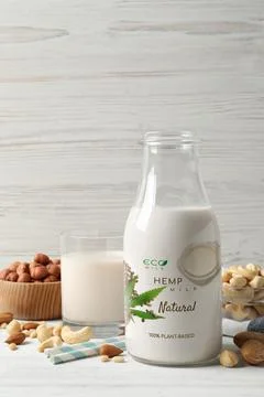 Glass and bottle of hemp milk and different nuts on white wooden table. Vegan Stock Photos