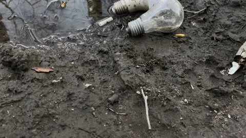 Glass and energy-saving light bulbs are thrown out into the dirt and puddles on  Stock Footage 130791289