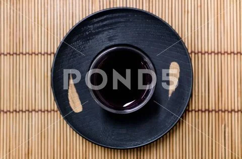 Glass and saucer on a black wooden coaster. Japanese glass with some tea insi Stock Photos