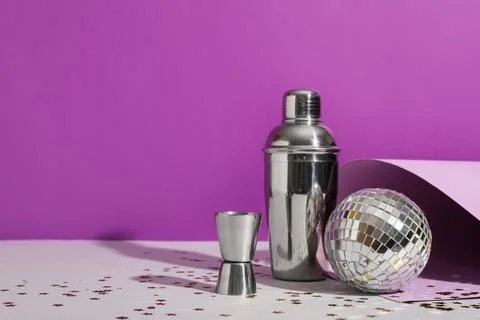 Glass, bartender tools and disco ball on white table near purple wall Stock Photos