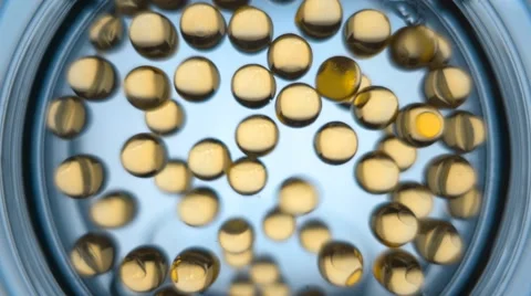 In a glass beaker fall transparent yellow balls of fish oil. Slow mo, slo mo Video stock 64713097