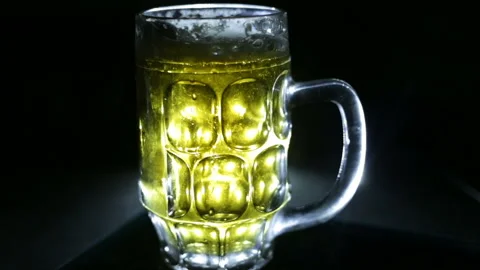 A glass of beer appears on the table in the dark and shines from within. Highlig Stock Footage 93208965