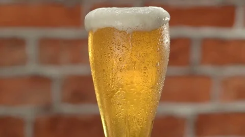 Glass of beer with froth and water drops over brick wall Stock Footage