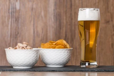 Glass of beer, golden chips and  pistachios in bowl Stock Photos