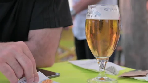 A glass of beer on a table in a cafe. A man chooses food from the menu and a Stock Footage 229872143