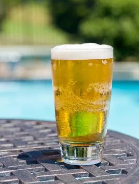 Glass of beer on table by poolside Plain pint glass of cold lager beer sit... Stock Photos
