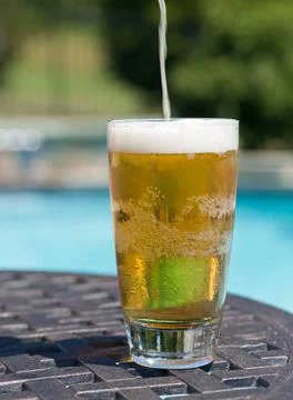 Glass of beer on table by poolside Plain pint glass of beer being poured s... Stock Photos
