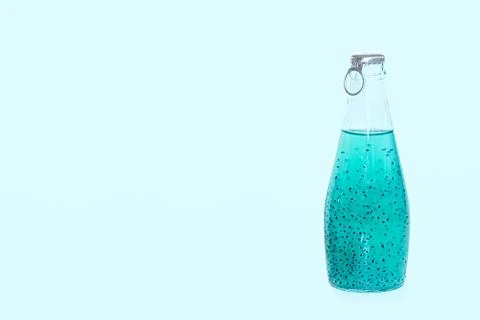 A glass bottle with blue basil seed stands on a blue background. Stock Photos