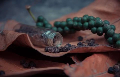 A glass bottle is next to many tiny green beads that resemble berries Foto stock