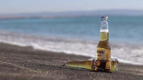 Glass bottles of Corona Extra in foam from the sea wave on dark sand Video stock 342797334