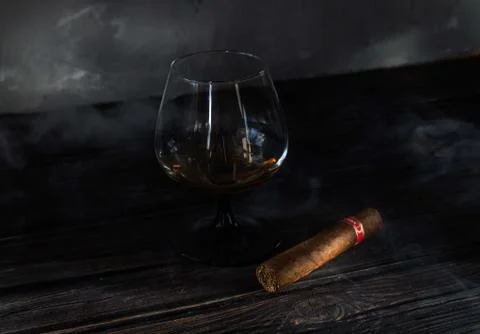 Glass of brandy and cuban cigar on an old wooden table. Stock Photos