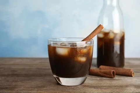 Glass of coffee with ice cubes on table against color background Stock Photos