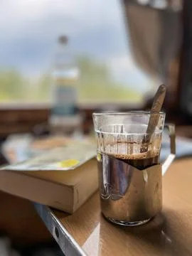 Glass of coffee stands on train table with book and water bottle in backgroun Stock Photos