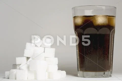 A glass of coke and a heap of sugar cubes Stock Photos
