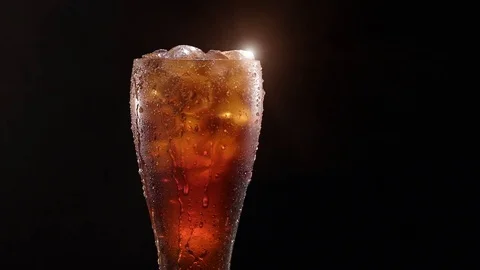 Glass with cola with ice rotating around its own axis on a black background. . Stock Footage 77036443