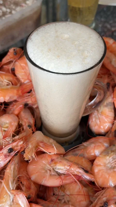 Glass of cold beer with boiled shrimp on black plate, foamy lager overflowing Stock Footage 345177786