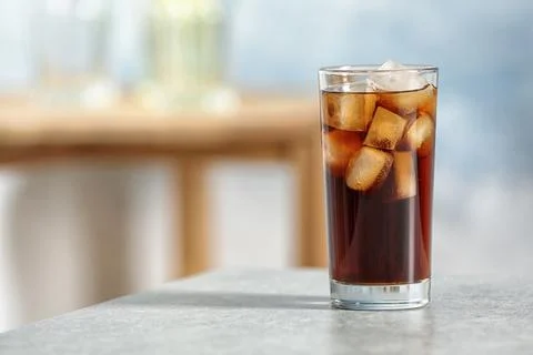 Glass of cold cola on table against blurred background. Space for text Stock Photos