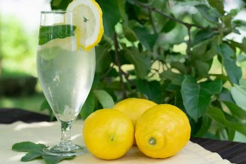A glass of cold lemonade with mint on the table with yellow lemons in the sum Stock Photos