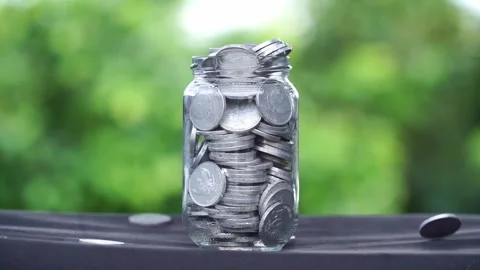 A glass container full filled with stacks of coins and some coins rained Stock Footage 287443448