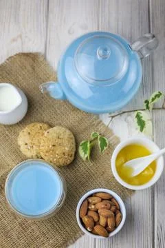 A glass cup and tea pot of blue Anchan Tea, cookies, milk,honey,almond. Stock Photos