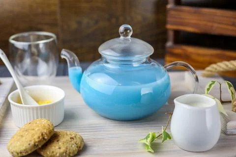 A glass cup and tea pot of blue Anchan Tea, cookies, milk,honey,almond. Stock Photos