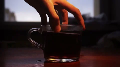 Glass cup full of tea is being put on a wooden table with a widow on background 스톡 동영상 168248384