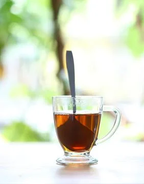 Glass cup of tea with spoon on a table in sunlight Stock Photos