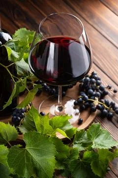 A glass of deep red wine with ripe grapes and fresh green vine leaves on a .. Stock Photos