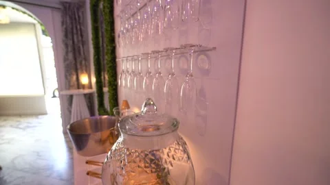 Glass drink dispenser below a wall of hanging champagne flutes Stock Footage 345549351