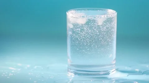 Glass of drinking water with bubbles, water is pouring, blue studio background Stock Footage 164712910