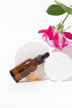 Glass dropper bottle on podium with rose flower. Stock Photos