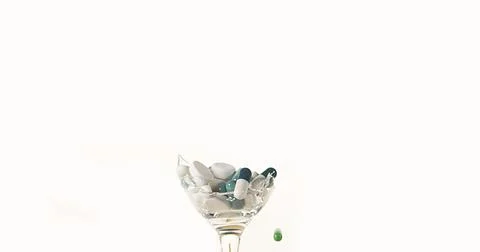 Glass filled with Capsules Exploding against White Background Foto stock