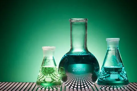 Glass flasks placed in a laboratory table with green liquid Stock Photos