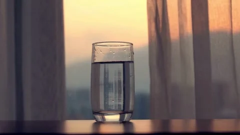 Glass of fresh water on table at sunset window Video stock 332276898