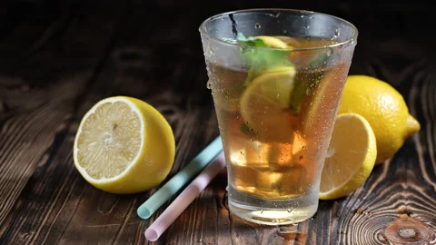 Glass of iced tea with ice cubes and sliced lemon, fresh mint on rustic wooden Stock Footage 155329379