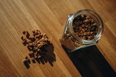 Glass jar of bee bread with granules spilled on a wooden table. Top view Stock Photos