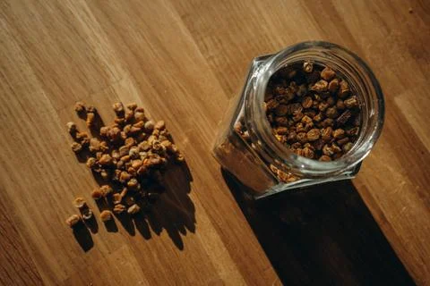 Glass jar of bee bread with granules spilled on a wooden table. Top view Stock Photos