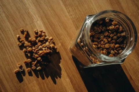 Glass jar of bee bread with granules spilled on a wooden table. Top view Stock Photos