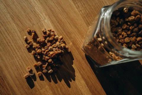 Glass jar of bee bread with granules spilled on a wooden table. Top view Stock Photos
