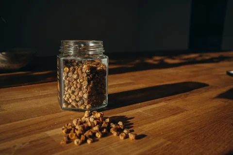 Glass jar of bee bread with granules spilled on a wooden table. Stock Photos