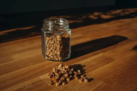 Glass jar of bee bread with granules spilled on a wooden table. Stock Photos