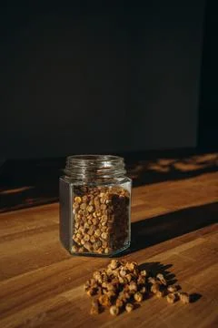 Glass jar of bee bread with granules spilled on a wooden table. Stock Photos
