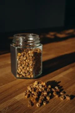 Glass jar of bee bread with granules spilled on a wooden table. Stock Photos