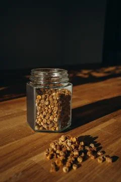 Glass jar of bee bread with granules spilled on a wooden table. Stock Photos